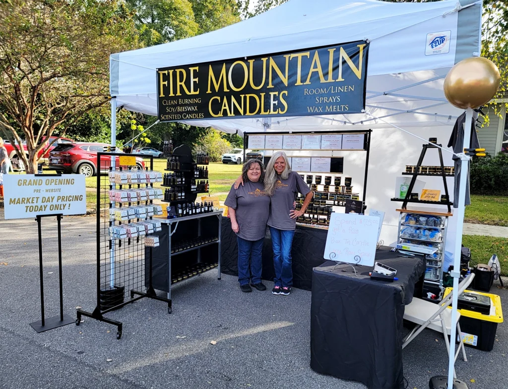Scented Candle and home fragrance products vendor market image depicting a large variety of premium candles, room-linen sprays and wax melts with two ladies in our Fire Mountain Candle's team.